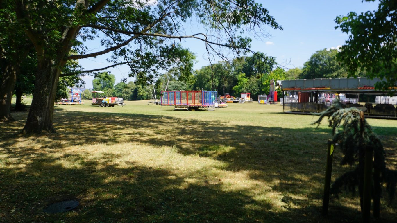 A sunny outdoor park with playground equipment and shaded trees.
