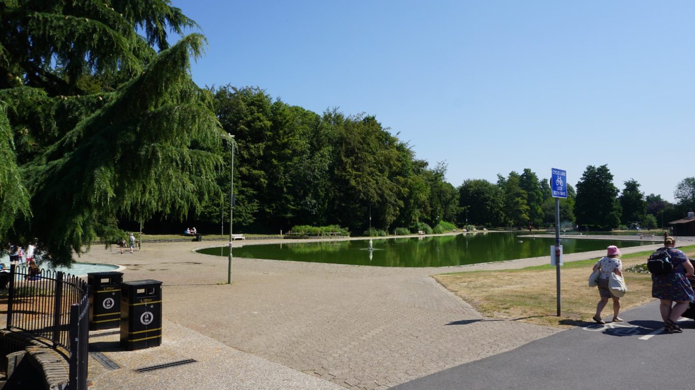A sunny park scene with trees, pathways, and people walking.